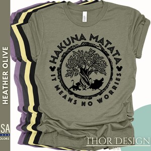 Puede incluir: Una camiseta verde con un gr&aacute;fico negro de un &aacute;rbol y el texto "Hakuna Matata It Means No Worries" en un c&iacute;rculo alrededor del &aacute;rbol.