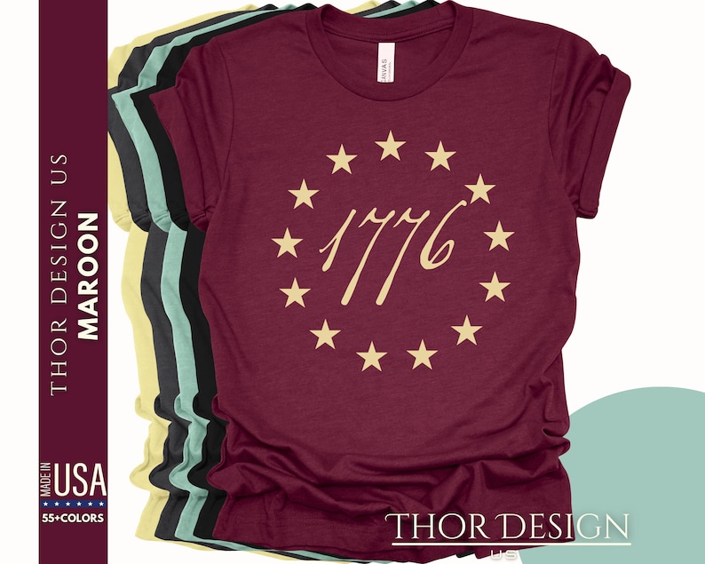 May include: Maroon t-shirt featuring a circle of gold stars and the text "1776" in a gold script font.