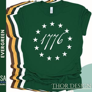 Pode incluir: Uma camiseta verde com um c&iacute;rculo branco de estrelas e o texto "1776" em uma fonte cursiva.