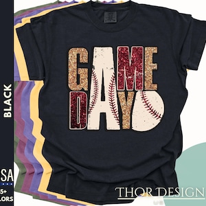 May include: A black t-shirt with the words "GAME DAY" in gold and red glitter with a baseball graphic. The shirt is made in the USA and available in 25+ colors.