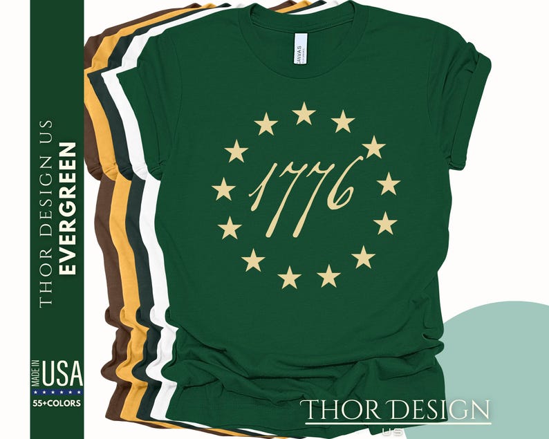 May include: A green t-shirt featuring a gold circle of stars and the text "1776" in a gold script font. The shirt is available in a range of colours.