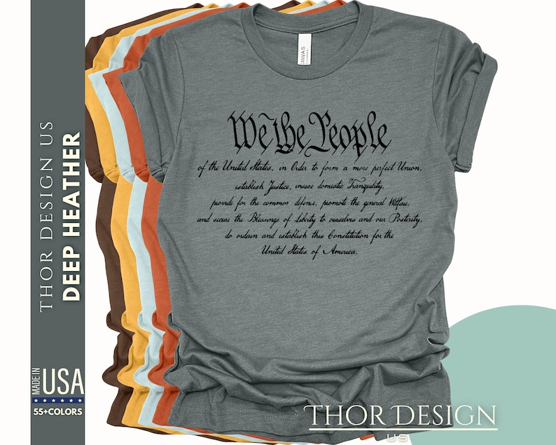 May include: A dark heather grey t-shirt with the text "We the People" and the preamble to the United States Constitution printed in black.
