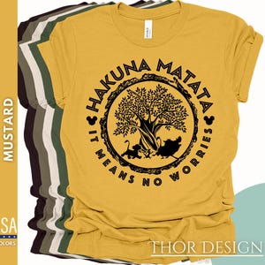 Puede incluir: Una camiseta amarilla mostaza con un gr&aacute;fico circular negro que presenta un &aacute;rbol, animales y el texto "Hakuna Matata It Means No Worries".