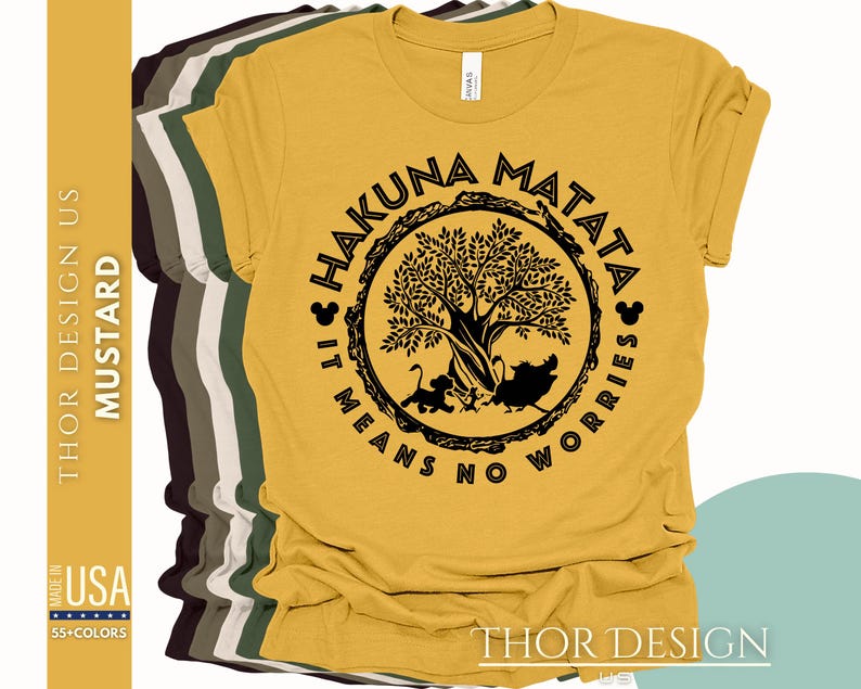 Puede incluir: Una camiseta amarilla mostaza con un gr&aacute;fico circular negro que presenta un &aacute;rbol, animales y el texto "Hakuna Matata It Means No Worries".