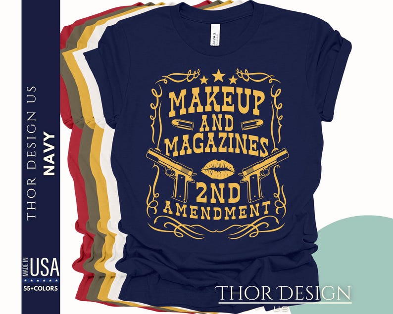 May include: Navy blue t-shirt with a gold graphic design featuring two guns crossed with a lipstick kiss and the text "Makeup and Magazines 2nd Amendment".
