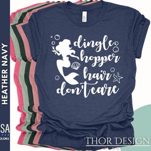 May include: A navy blue t-shirt with a white graphic of a mermaid with the text "dingle hopper hair don't care".