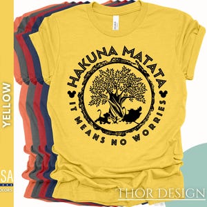Puede incluir: Camiseta amarilla con un gr&aacute;fico negro de un &aacute;rbol y el texto "Hakuna Matata It Means No Worries" en un c&iacute;rculo.