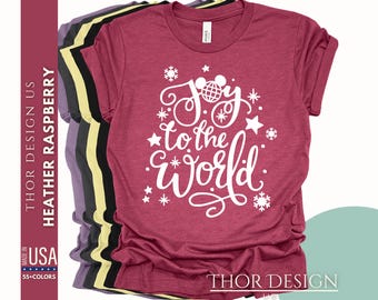 May include: A heather raspberry t-shirt with a white design that says "Joy to the World" with a stylized Mickey Mouse head and snowflakes.