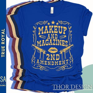 May include: Blue t-shirt with a gold graphic design that says "Makeup and Magazines 2nd Amendment". The graphic includes a lipstick kiss, two pistols, and bullets.
