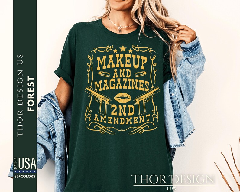 May include: A dark green t-shirt with a gold graphic design featuring two pistols, a lipstick kiss, and the text "Makeup and Magazines 2nd Amendment".