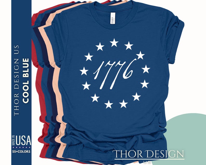 Pode incluir: Uma camiseta azul marinho com um c&iacute;rculo branco de estrelas ao redor do n&uacute;mero 1776. O texto "THOR DESIGN US" est&aacute; impresso na parte inferior da camiseta.