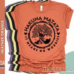 Puede incluir: Una camiseta naranja jaspeada con un gr&aacute;fico negro de un &aacute;rbol y el texto "Hakuna Matata It Means No Worries" en un c&iacute;rculo.