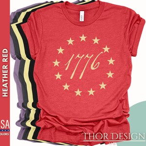 May include: Red heather t-shirt with a circle of stars and the number 1776 in a gold script font.