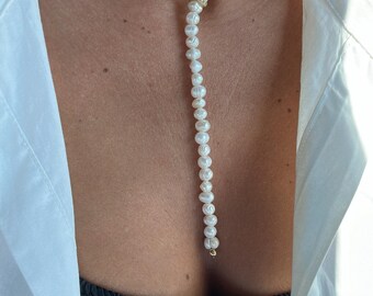 May include: A white pearl necklace with a long, dangling pearl strand. The necklace is layered and features a gold clasp.