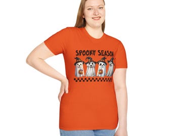 May include: Orange t-shirt featuring the words "Spooky Season" and a graphic of four cartoon ghosts wearing witch hats and holding pumpkins. The shirt has a black and white checkered border.