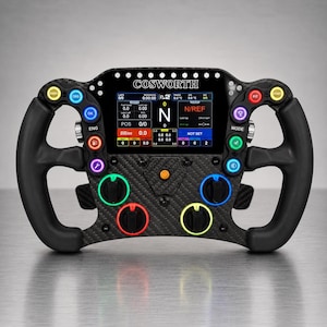 May include: A black carbon fibre racing steering wheel featuring a central digital display with the text COSWORTH. The wheel includes numerous multi-coloured buttons, rotary dials, and ergonomic grips, designed for high-performance vehicle control.
