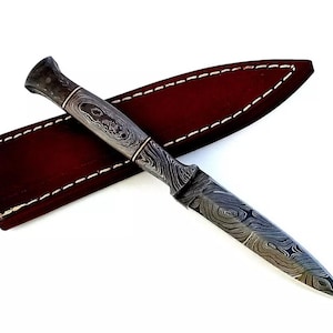 May include: A black and silver patterned dagger with a leather sheath. The dagger has a pointed tip and a textured handle.