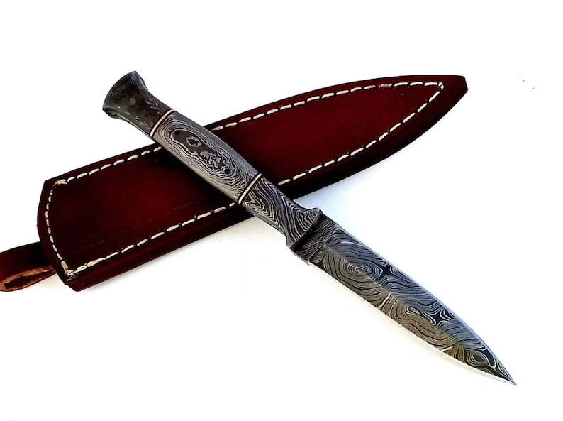 May include: A black and silver patterned dagger with a leather sheath. The dagger has a pointed tip and a textured handle.