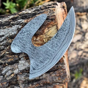 May include: A large, curved, silver knife with a patterned blade. The knife is resting on a piece of wood.