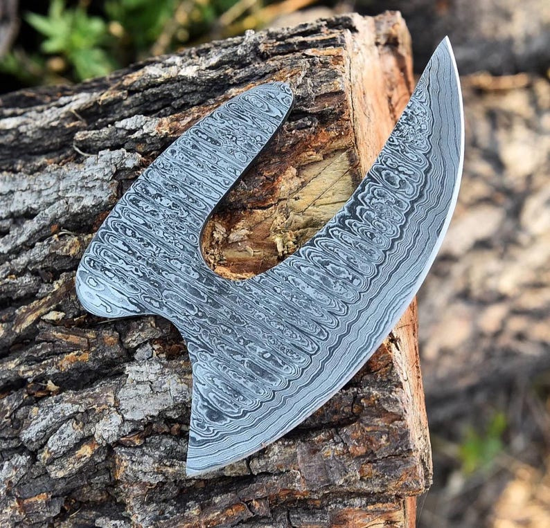 May include: A large, curved, silver knife with a patterned blade. The knife is resting on a piece of wood.