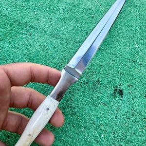 May include: A silver dagger with a white bone handle. The blade is long and pointed, and the handle is decorated with small dots.