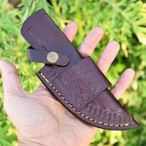 May include: A brown leather knife sheath with a decorative stitch pattern and a brass snap closure.