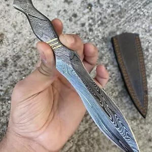 May include: A silver and blue patterned dagger with a gold accent. The dagger is held in a hand and has a sharp point.