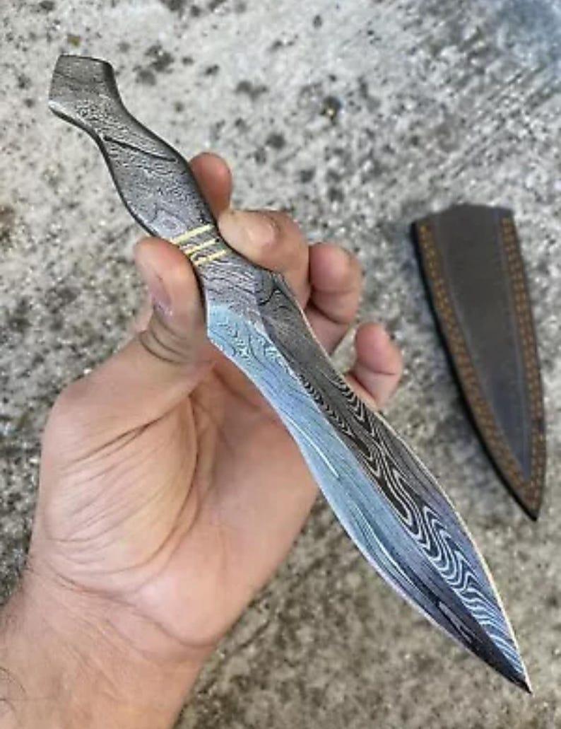 May include: A silver and blue patterned dagger with a gold accent. The dagger is held in a hand and has a sharp point.