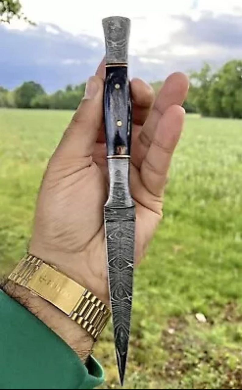 May include: A small, sharp knife with a patterned steel blade and a dark blue handle. The blade is about 6 inches long and has a pointed tip. The handle is made of wood and has a decorative design.