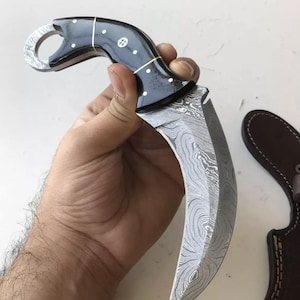 May include: A black and white patterned handle with a ring on the top, attached to a silver, curved, Damascus steel blade.
