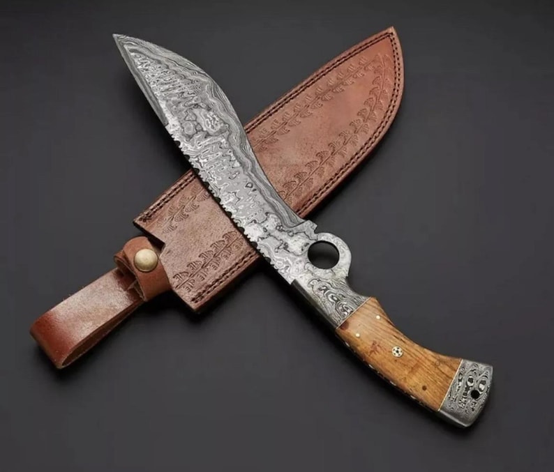 Op de afbeelding: Een Damascus staal mes met een bruine leren schede. Het mes heeft een houten handvat en een decoratief patroon op het lemmet.