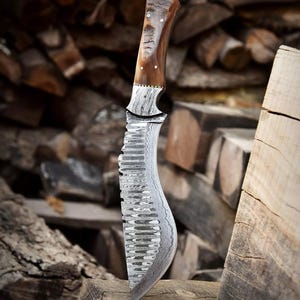 Op de afbeelding: Een Damascus stalen mes met een bruine houten handvat. Het blad heeft een golvend patroon en een gekartelde rand. Het mes ligt op een stuk hout.