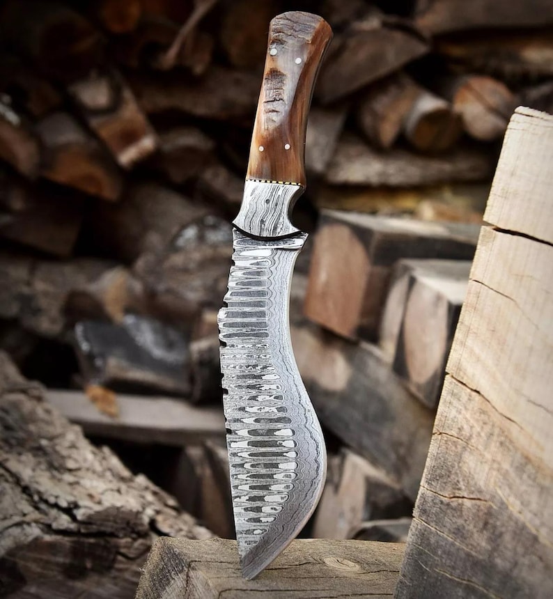 Op de afbeelding: Een Damascus stalen mes met een bruine houten handvat. Het blad heeft een golvend patroon en een gekartelde rand. Het mes ligt op een stuk hout.
