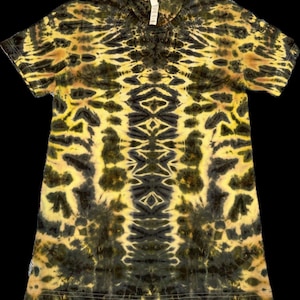 May include: A short-sleeved t-shirt with a tie-dye pattern in shades of yellow and black. The design features symmetrical, organic shapes and patterns, creating a visually striking and unique look. The shirt has a crew neck and a tag visible at the neckline.