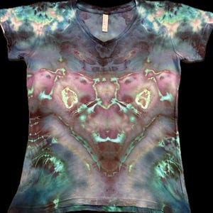 May include: A short-sleeved V-neck t-shirt with a tie-dye pattern in shades of blue, purple, and teal. The design features symmetrical patterns and a soft, blended colour palette. The shirt has a relaxed fit.