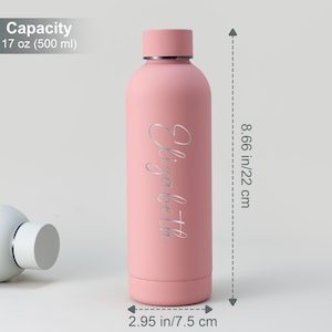 May include: A pink insulated water bottle with the name "Elizabeth" in a silver script. The bottle is 8.66 inches (22 cm) tall and 2.95 inches (7.5 cm) wide, with a capacity of 17 oz (500 ml).