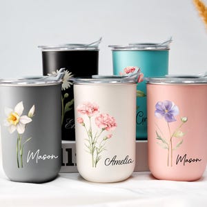 Op de afbeelding: Een verzameling ge&iuml;soleerde bekers in verschillende kleuren, waaronder grijs, zwart, blauwgroen, cr&egrave;me en roze. Elke beker heeft een bloemenontwerp en een naam in script. De bekers hebben zilveren deksels en zijn ontworpen voor dranken.
