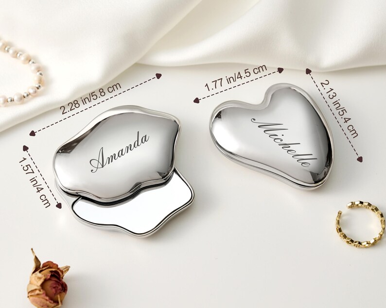 May include: Two silver compact mirrors. One is an irregular shape, 2.28 in (5.8 cm) long, with "Amanda" engraved. The other is heart-shaped, 2.13 in (5.4 cm) long, with "Michelle" engraved. Both have a mirror inside.