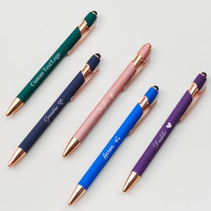 May include: A selection of personalised pens in shades of green, navy, pink, blue, and purple. Each pen has a rose gold trim and a unique inscription, including "Custom Text/Logo", "Grandma", "Saylor", "Aaron", and "Daddie".