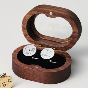 May include: A wooden oval-shaped box with a clear top, holding two silver cufflinks. One cufflink has the initials "K.R" and the date "25.08.29". The other cufflink says "Forever and Always".