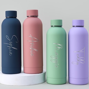 May include: Four colorful, personalized water bottles. The bottles are navy blue, pink, mint green, and lavender. Each bottle has a silver script name: Sophia, Archie, Maggie, and Teddy. The bottles are cylindrical with matching colored lids.