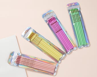 May include: Several packs of pencils in various colors, including pink, yellow, and green, are displayed. Each pack is sealed in a holographic bag. The pencils have text that reads "Good Vibes Only" and "Samuel".