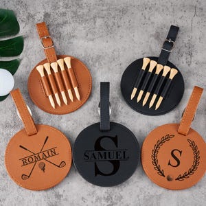 Può includere: Set di sei portachiavi per sacca da golf personalizzati con cinturini in similpelle e design diversi. I portachiavi presentano una mazza da golf, un monogramma e una ghirlanda con una lettera. I portachiavi sono marroni con accenti neri e bianchi.