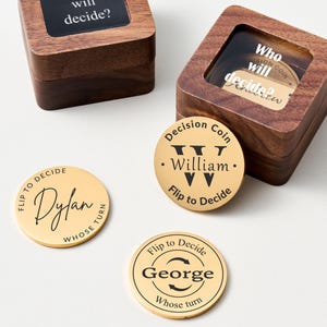 May include: Wooden boxes with clear tops containing decision coins. Gold-colored decision coins with names like "Dylan," "William," and "George" are scattered around. The coins have text like "Flip to Decide" and "Whose Turn."