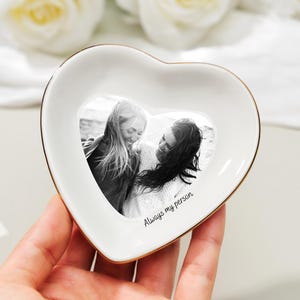 May include: A heart-shaped white ceramic trinket dish with a gold rim. The dish features a black and white photo of two people and the text "Always my person".