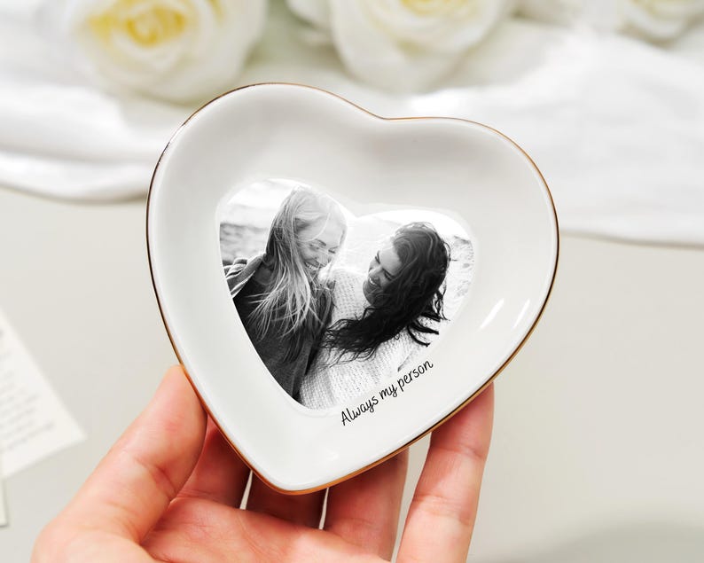 May include: A heart-shaped white ceramic trinket dish with a gold rim. The dish features a black and white photo of two people and the text "Always my person".