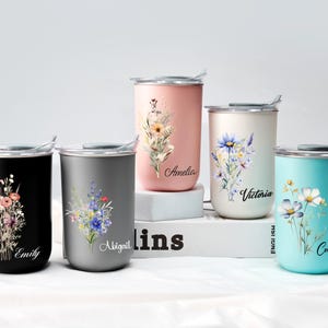 Op de afbeelding: Vijf roestvrijstalen reisbekers in zwart, grijs, roze, cr&egrave;me en turquoise. Elke beker heeft een bloemenontwerp en een naam: Emily, Abigail, Amelia, Victoria en Colleen. De bekers hebben zilveren deksels en staan op een wit oppervlak.