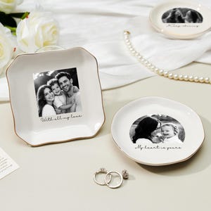 May include: White ceramic trinket dishes with gold trim, featuring black and white family photos. One dish is square with the text "With all my love." Another is round with the text "My heart is yours." Two rings are in the foreground.