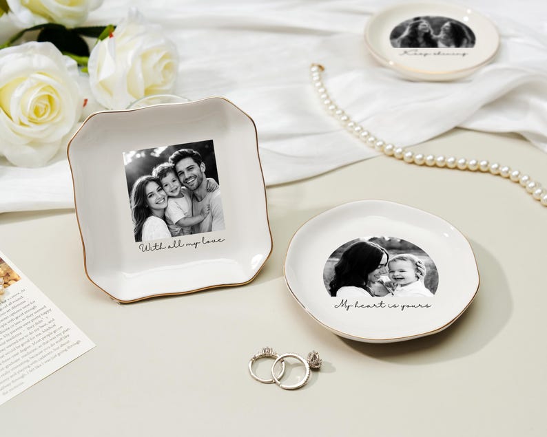 May include: White ceramic trinket dishes with gold trim, featuring black and white family photos. One dish is square with the text "With all my love." Another is round with the text "My heart is yours." Two rings are in the foreground.