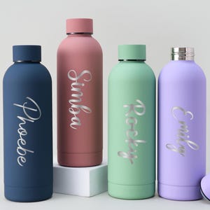 May include: Four insulated water bottles in navy blue, dusty rose, mint green, and lavender. Each bottle has a silver name inscription: Phoebe, Simba, Rocky, and Emily. The bottles have matching colored lids.